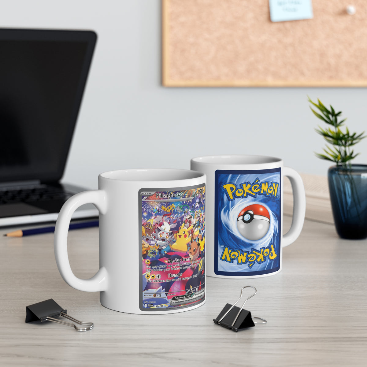 Two mugs on a desk displaying the front and back of the Pikachu ex celebration design beside a laptop and potted plant.